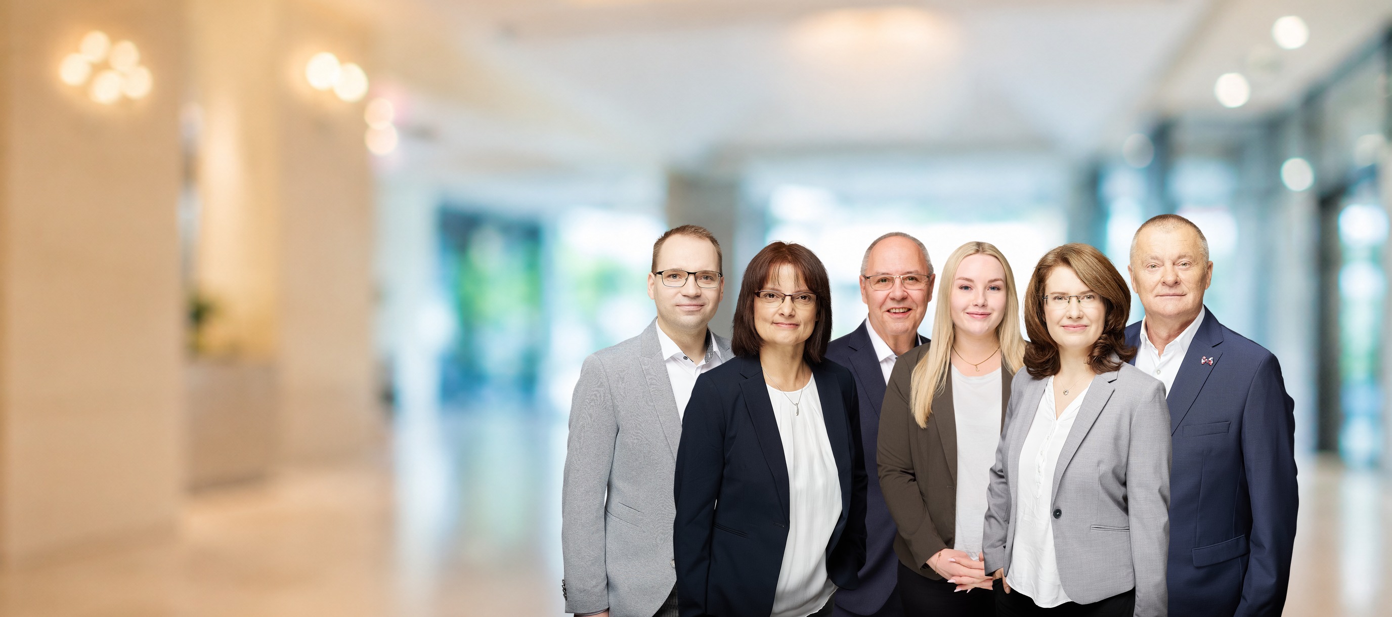 Das sechsköpfige Team von Fuhrmann Versicherungsmakler nebeneinander vor dem hellen Büro-Foyer